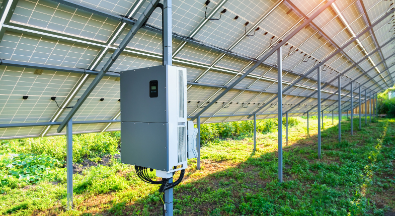 Inversor solar instalado bajo una estructura de paneles solares en un campo verde, capturando la eficiencia energética de las energías renovables.